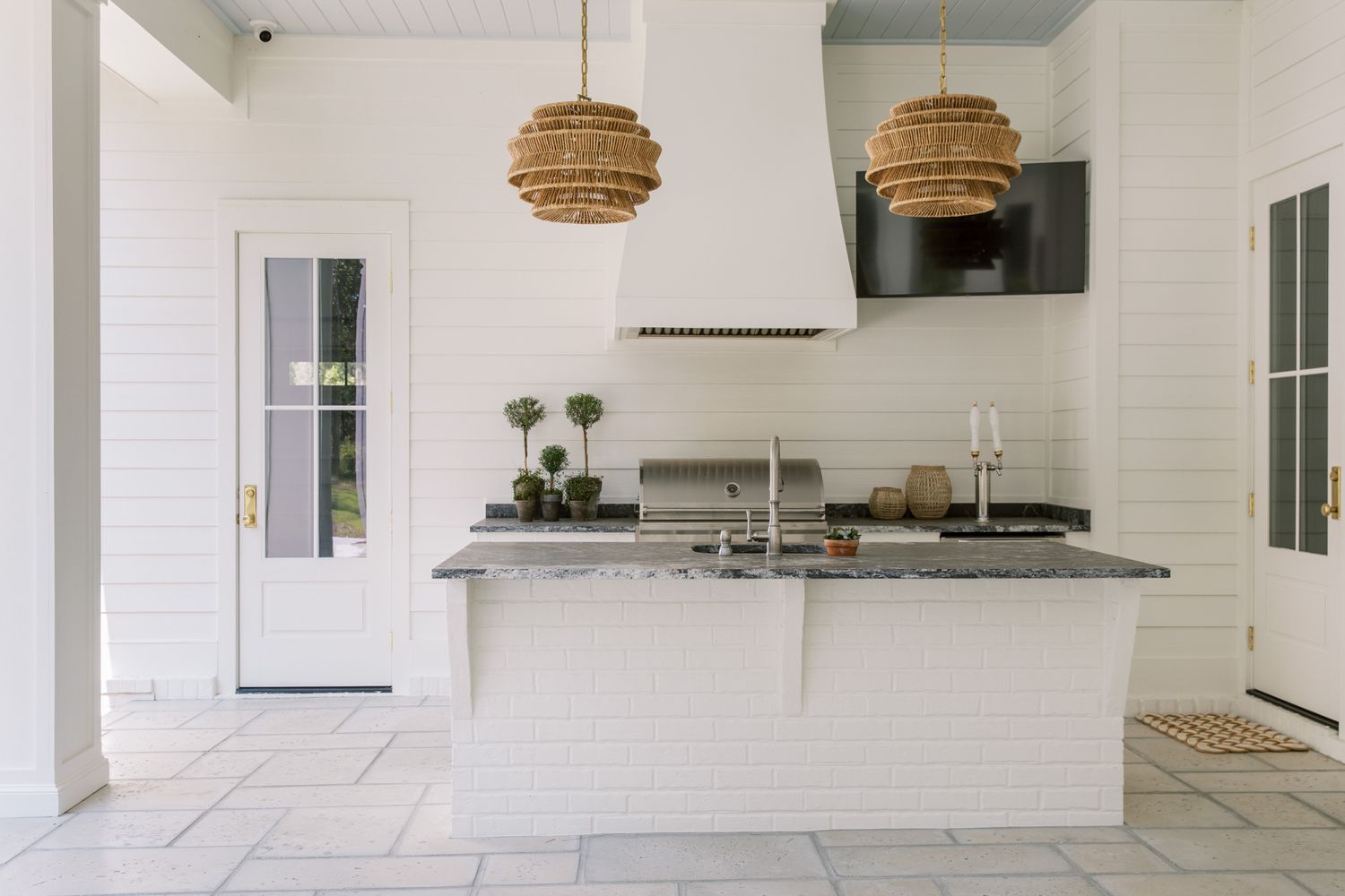 an outdoor kitchen containing a white brick island with a dark stone top and woven lanterns suspended overhead