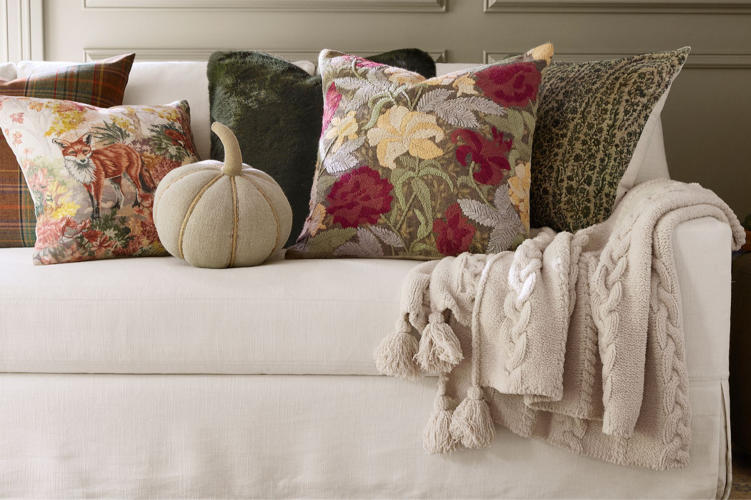 A couch with decorative pillows a small fabric pumpkin and a textured throw blanket draped over the side