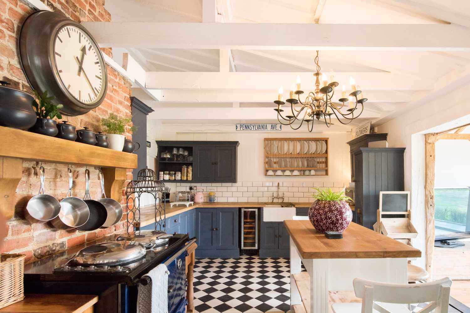 A modern farmhouse kitchen with a central wooden island black cabinetry brick accent wall and chandelier featuring checkered flooring