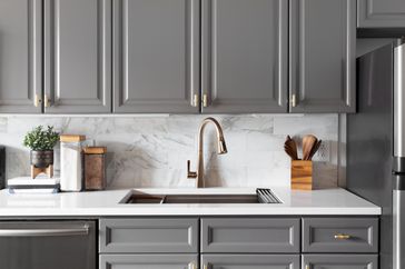 Modern kitchen interior with gray cabinets marble backsplash and a metallic faucet over a white countertop