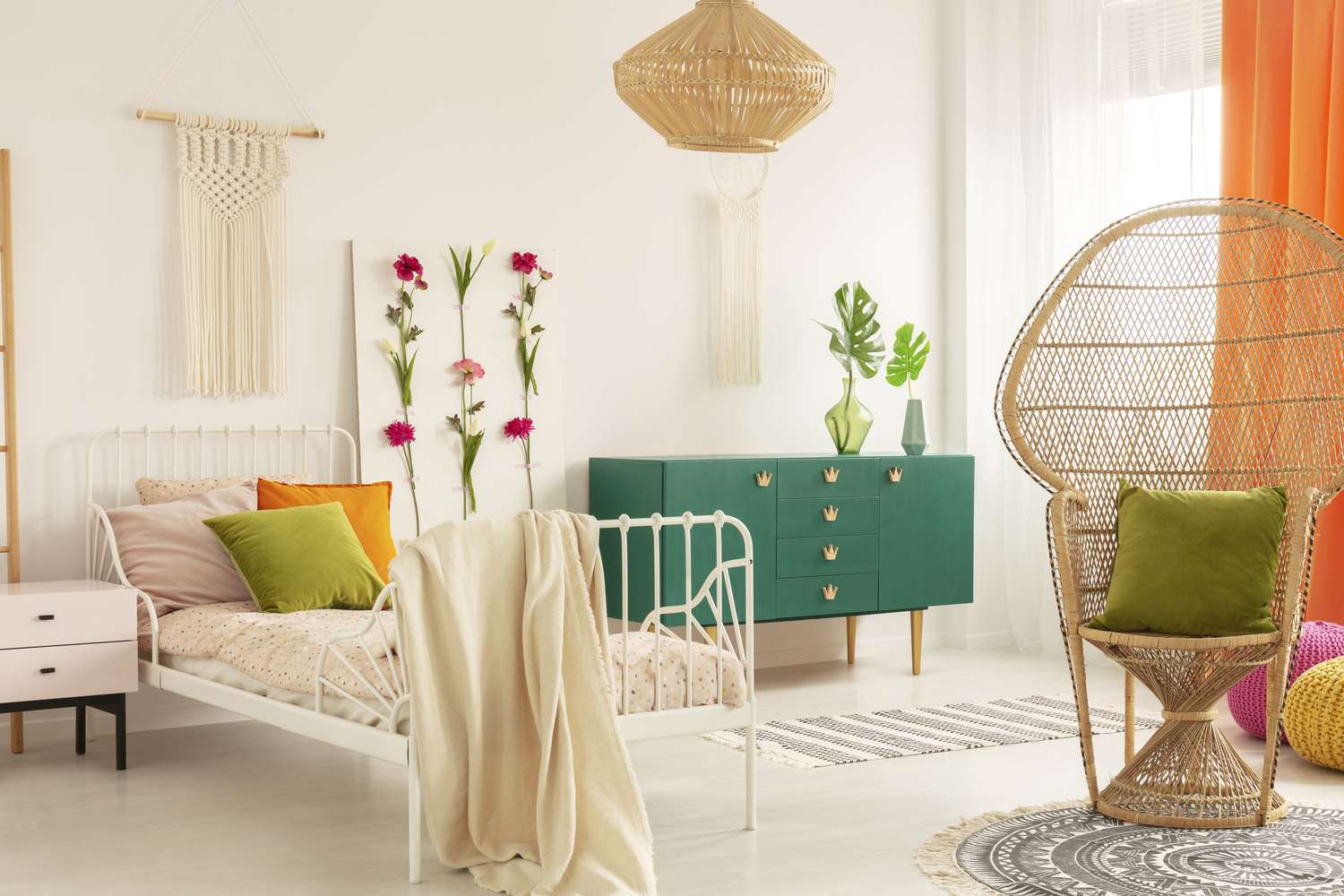 A decorated bedroom with a wicker armchair a green chest of drawers and wallmounted decorations