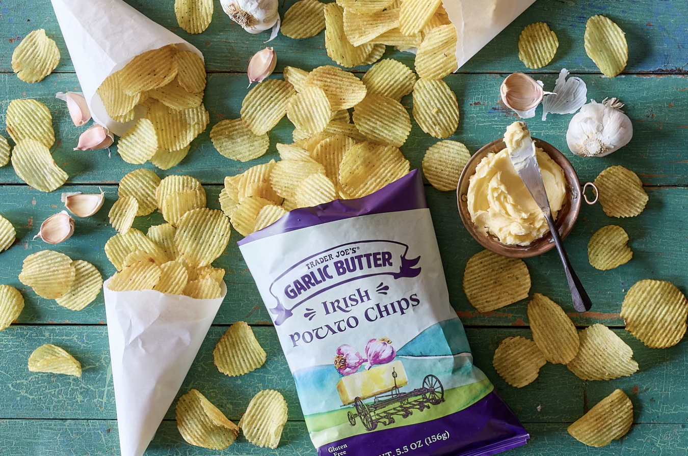 Trader Joes Garlic Butter Irish Potato Chips on a table with scattered chips and garlic cloves