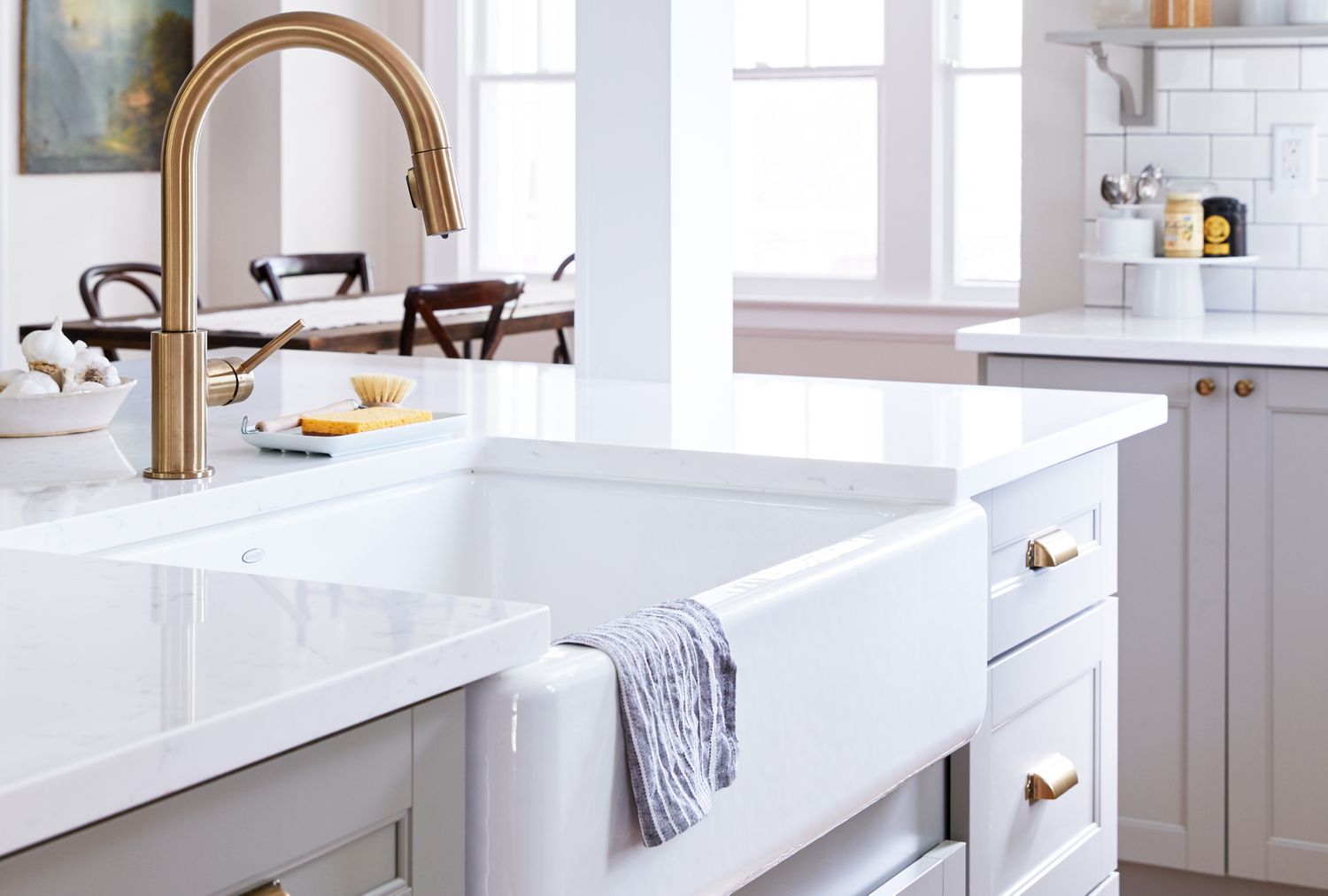 Farmhousestyle kitchen sink with a towel draped over the front surrounded by a bright kitchen with white countertops