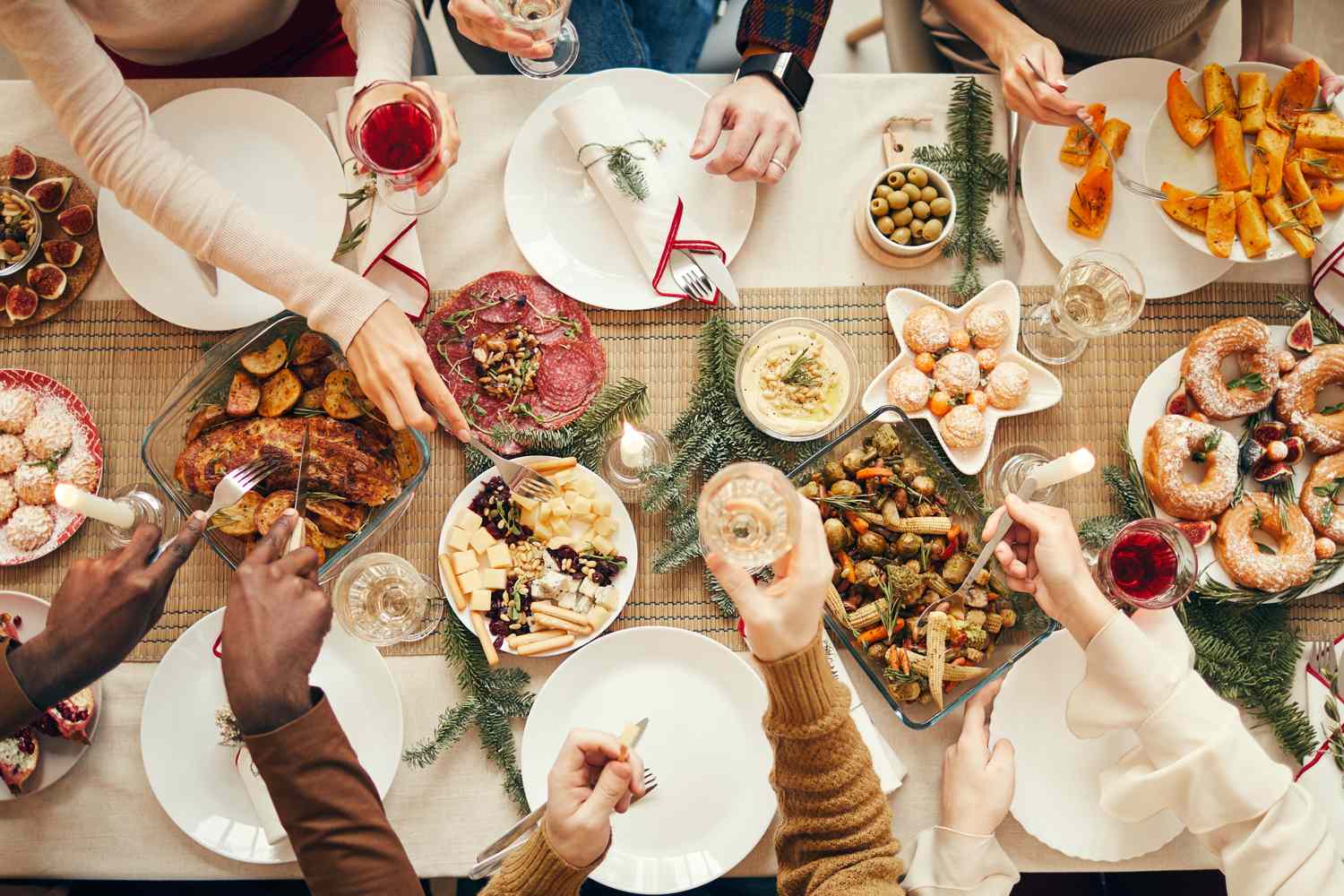 People reaching for food and drinks at a festive dinner gathering surrounded by various holiday dishes