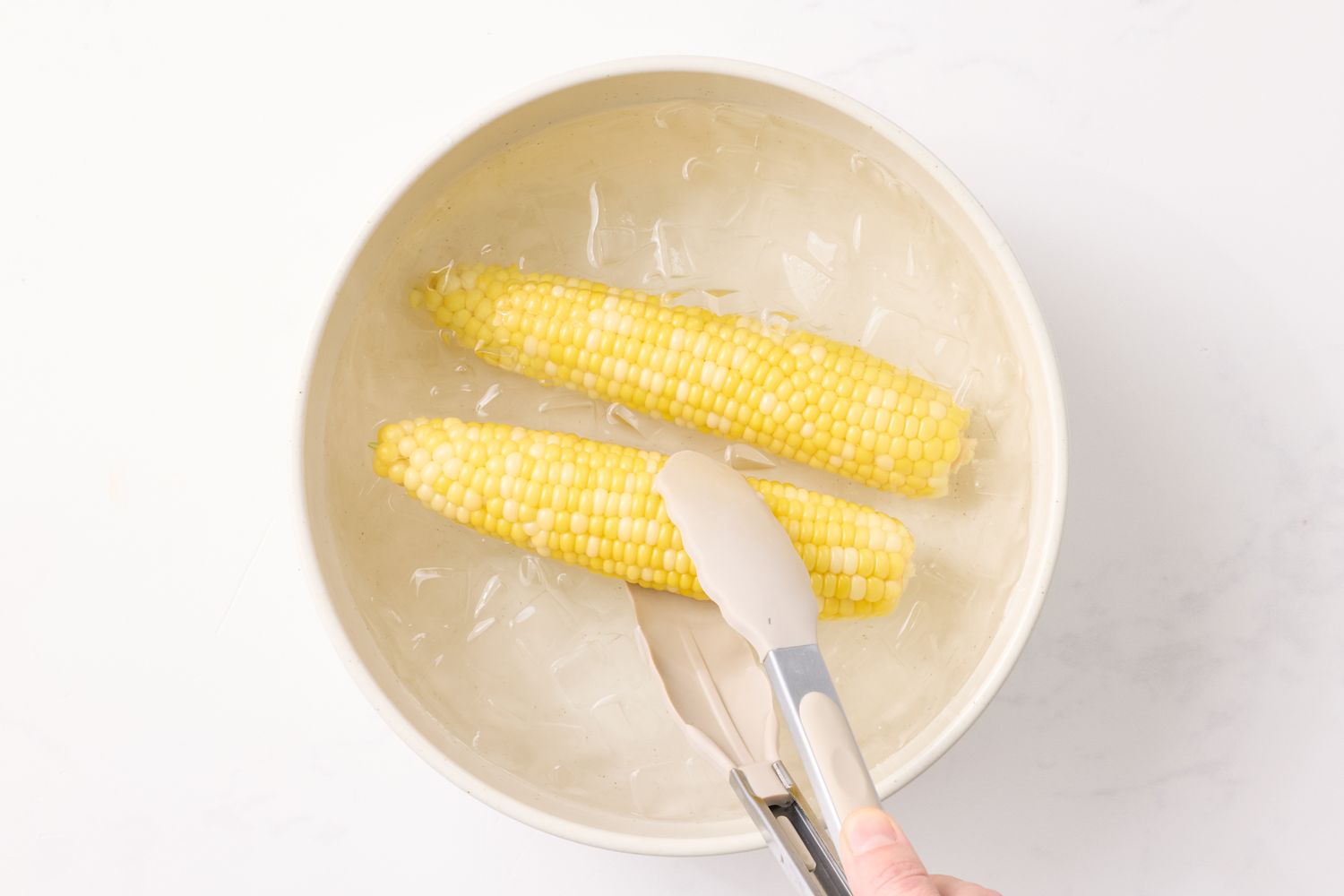 Corn being placed in ice water with tongs