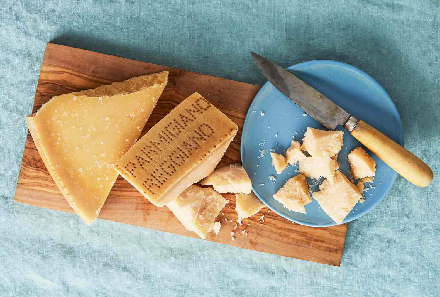Pieces of Parmigiano Reggiano cheese on a wooden board with a knife on a blue plate