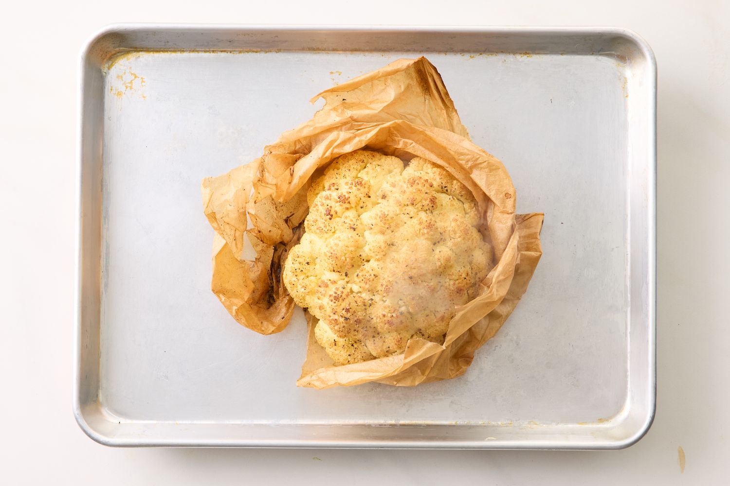 A whole roasted cauliflower wrapped in parchment paper on a baking sheet