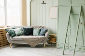 Interior of a cozy living room with a sofa, cushions, a wooden cabinet, and a ladder