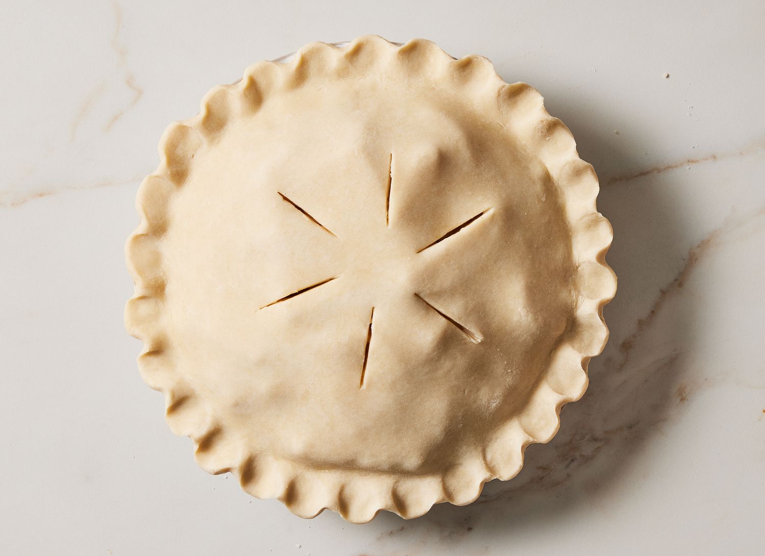 raw pie with pinched edges and venting slits on a marble surface