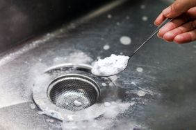 hand holding spoon with baking powder over a stainless steel sink and drian