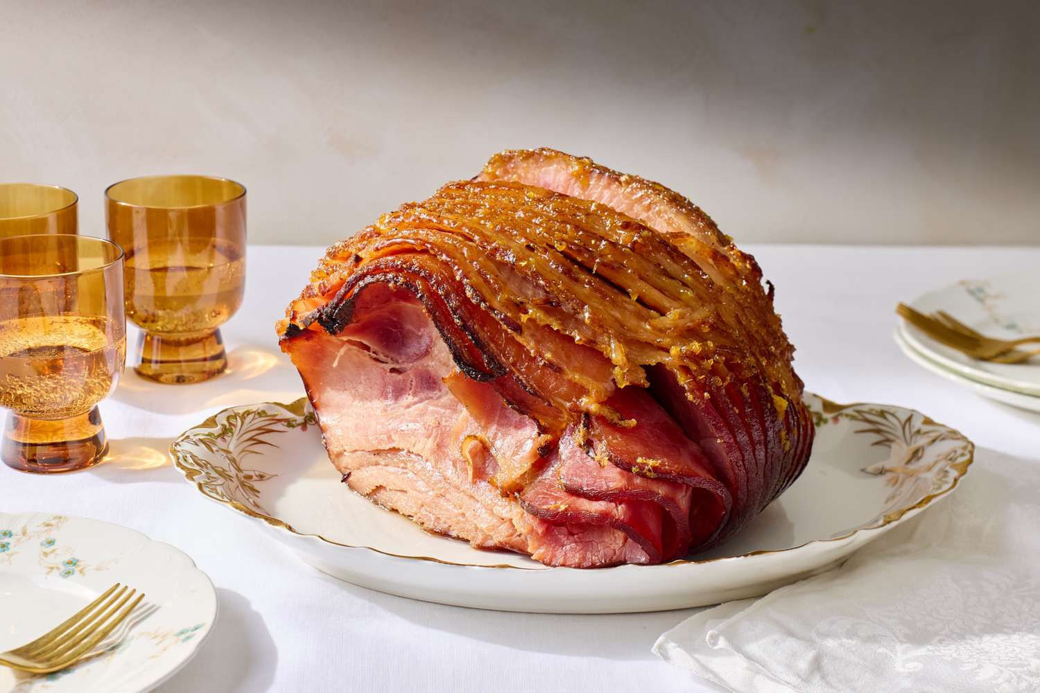 A honeyglazed spiral ham on a decorative plate placed on a table with glasses and plates