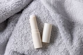 A lip balm tube with its cap removed, placed on a soft textured surface