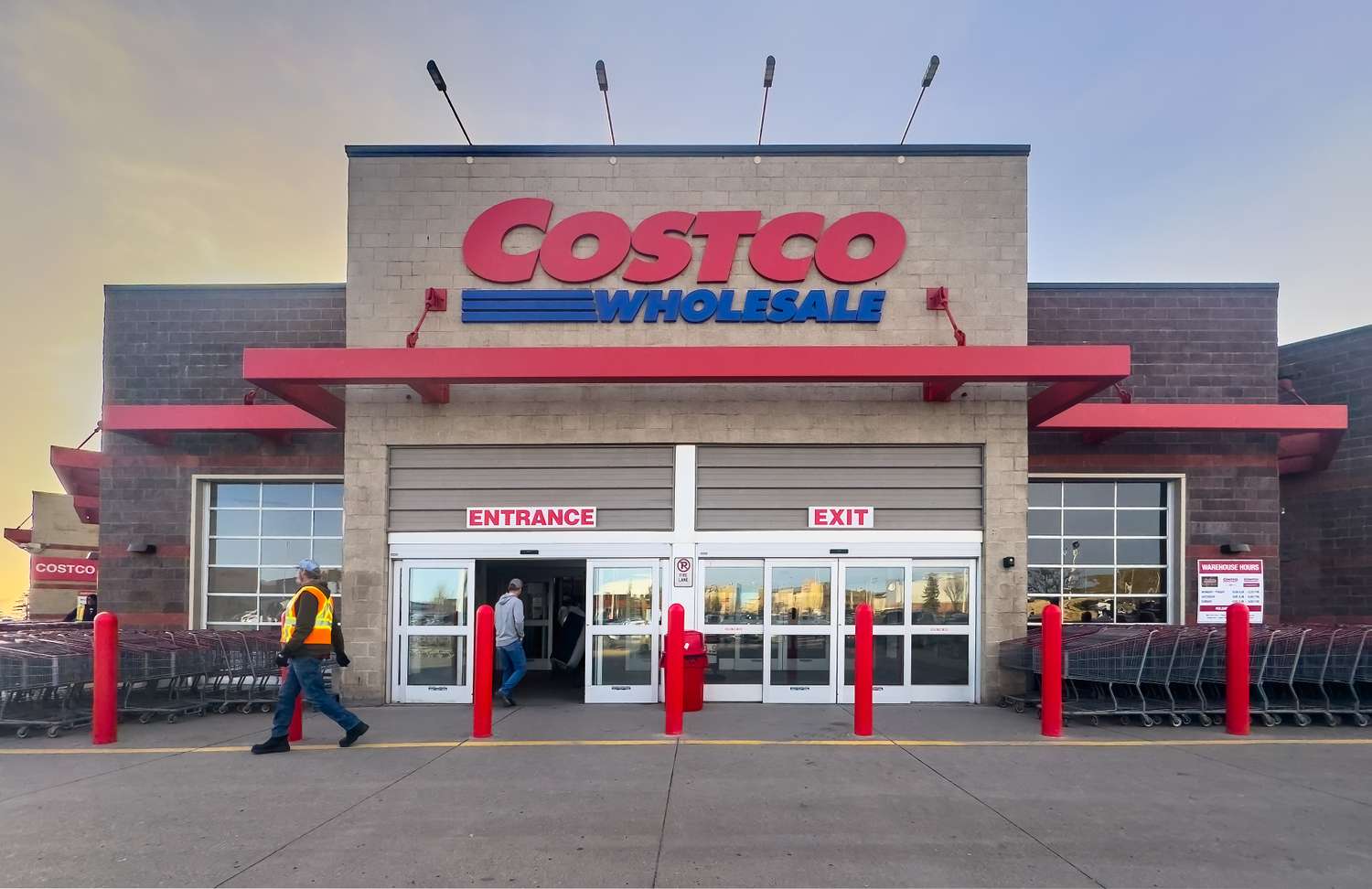 Exterior shot of a Costco Wholesale store at dusk with Costco Wholesale signage and people entering, exiting.