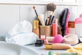 A bathroom counter with makeup items brushes powder and a pack of wipes among other cosmetic accessories