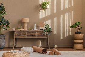 A meditation space with a wooden console table a yoga mat cushions potted plants and a small statue on the table