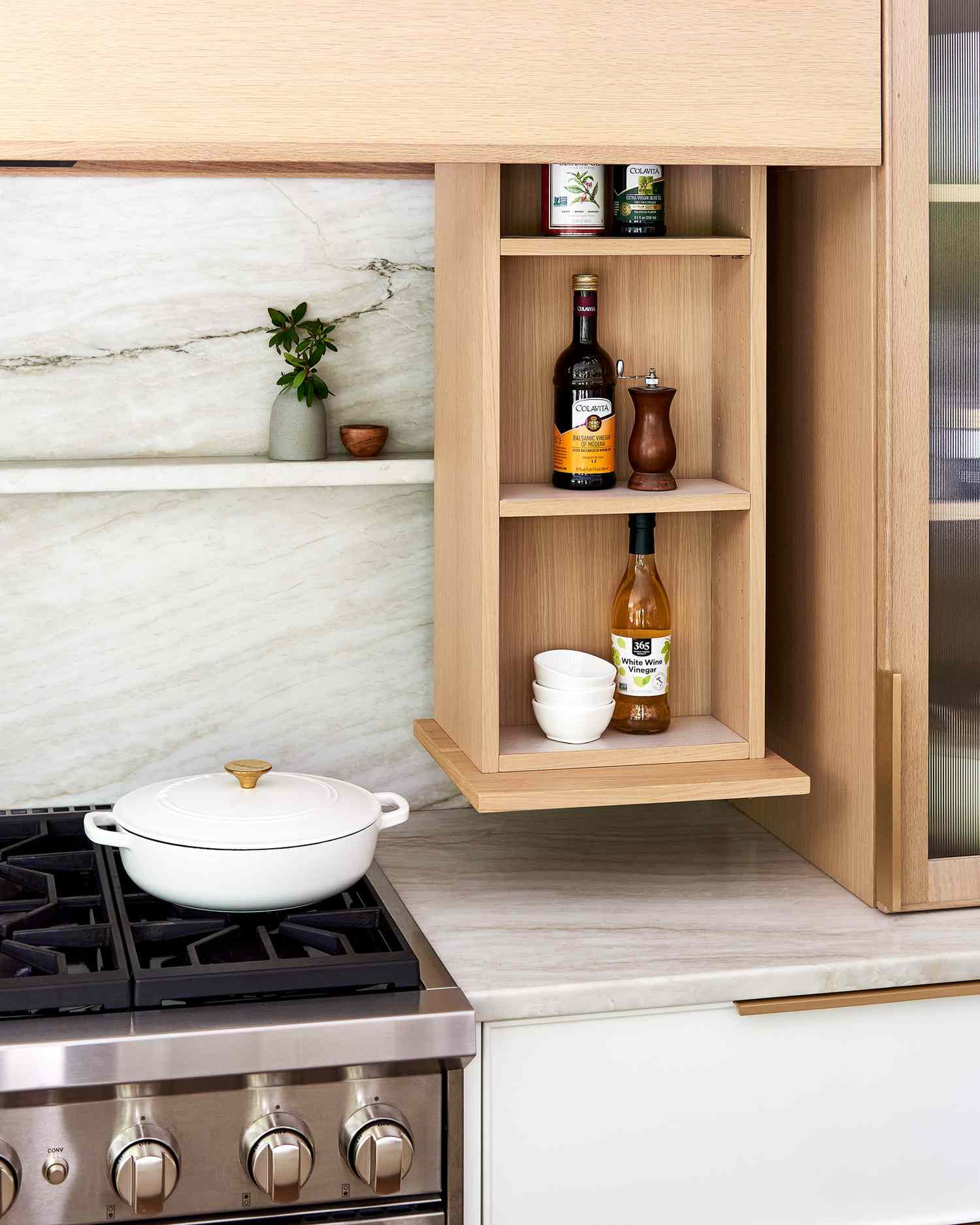 Kitchen interior showing a stovetop a white pot and a wooden cabinet with an integrated pullout spice rack