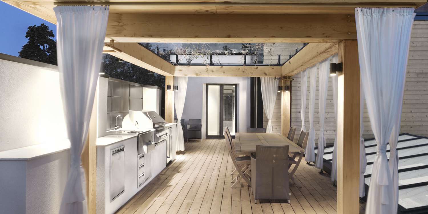 a rooftop patio with white curtains and an outdoor kitchen