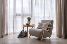Elegant grey armchair standing near coffee table with home decor and plaid in basket. Light and modern space in an urban apartment. New furniture in living room