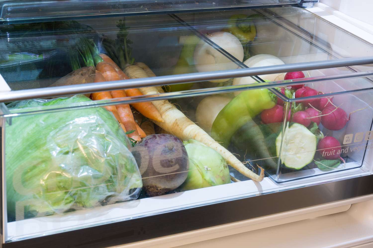 A refrigerator crisper drawer containing various fresh vegetables including carrots radishes and lettuce
