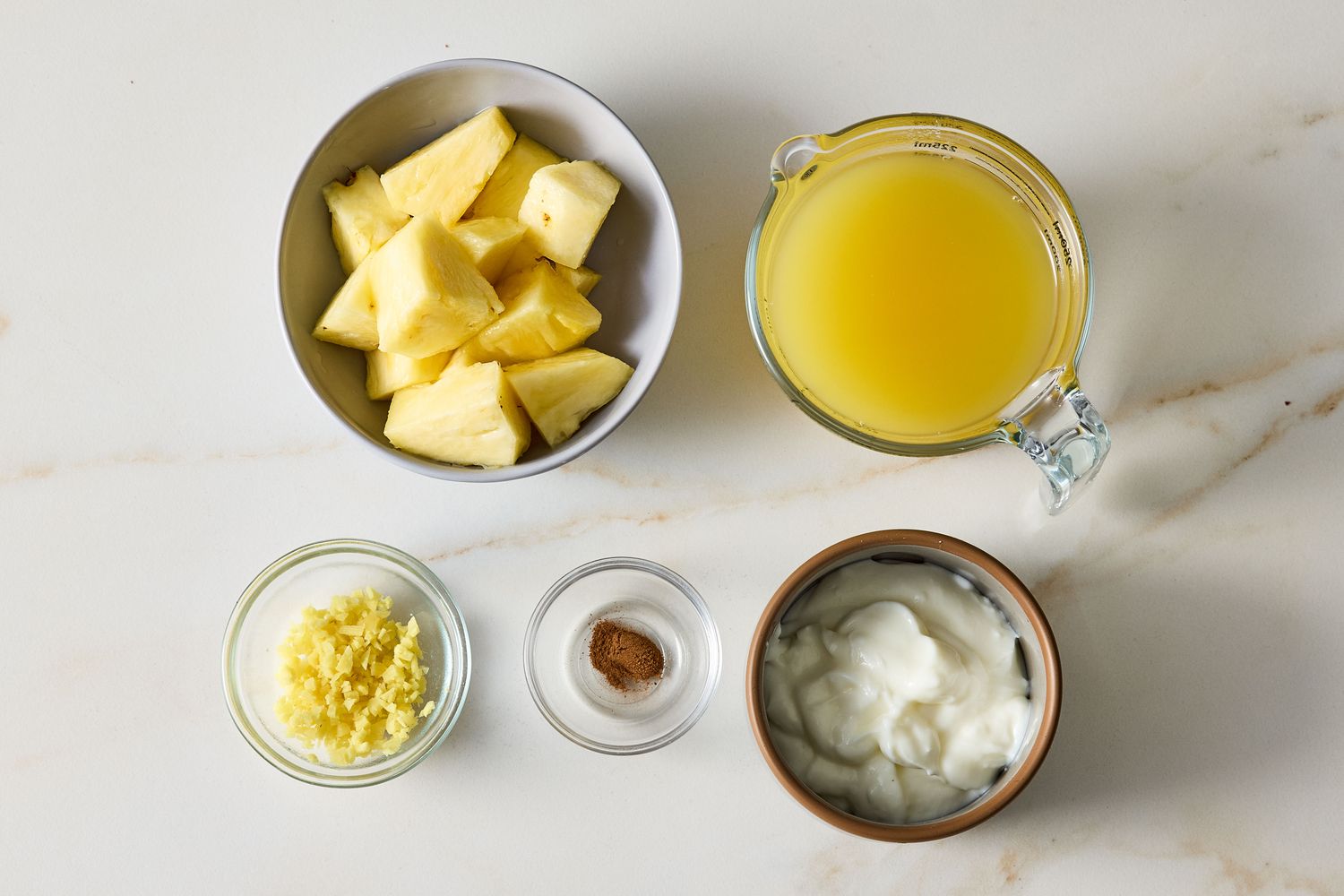 Ingredients laid out for a pineapple and ginger smoothie including pineapple chunks ginger juice yogurt and spices
