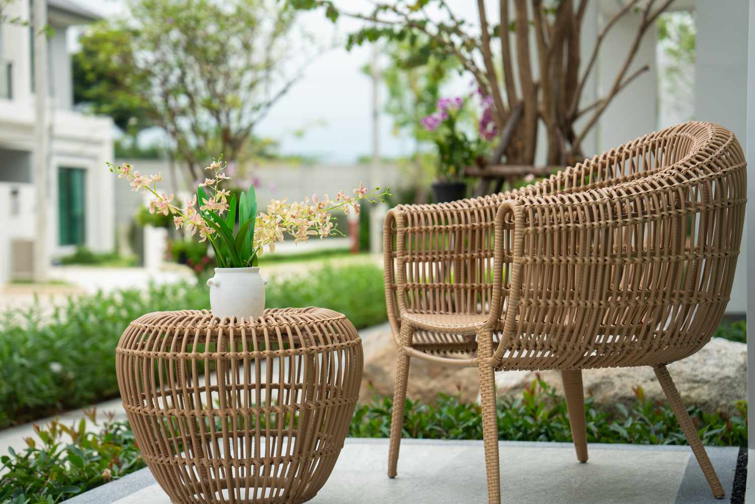 Outdoor seating area with a wicker chair and table potted flowers on the table lush greenery in the background