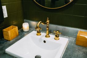 Bathroom sink with a brass faucet candle and wooden containers on a gray countertop