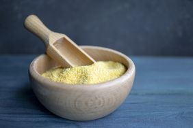 A wooden bowl filled with yellow grainy substance accompanied by a small wooden scoop resting on top