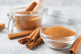 Cinnamon powder in a bowl on a textured wooden background