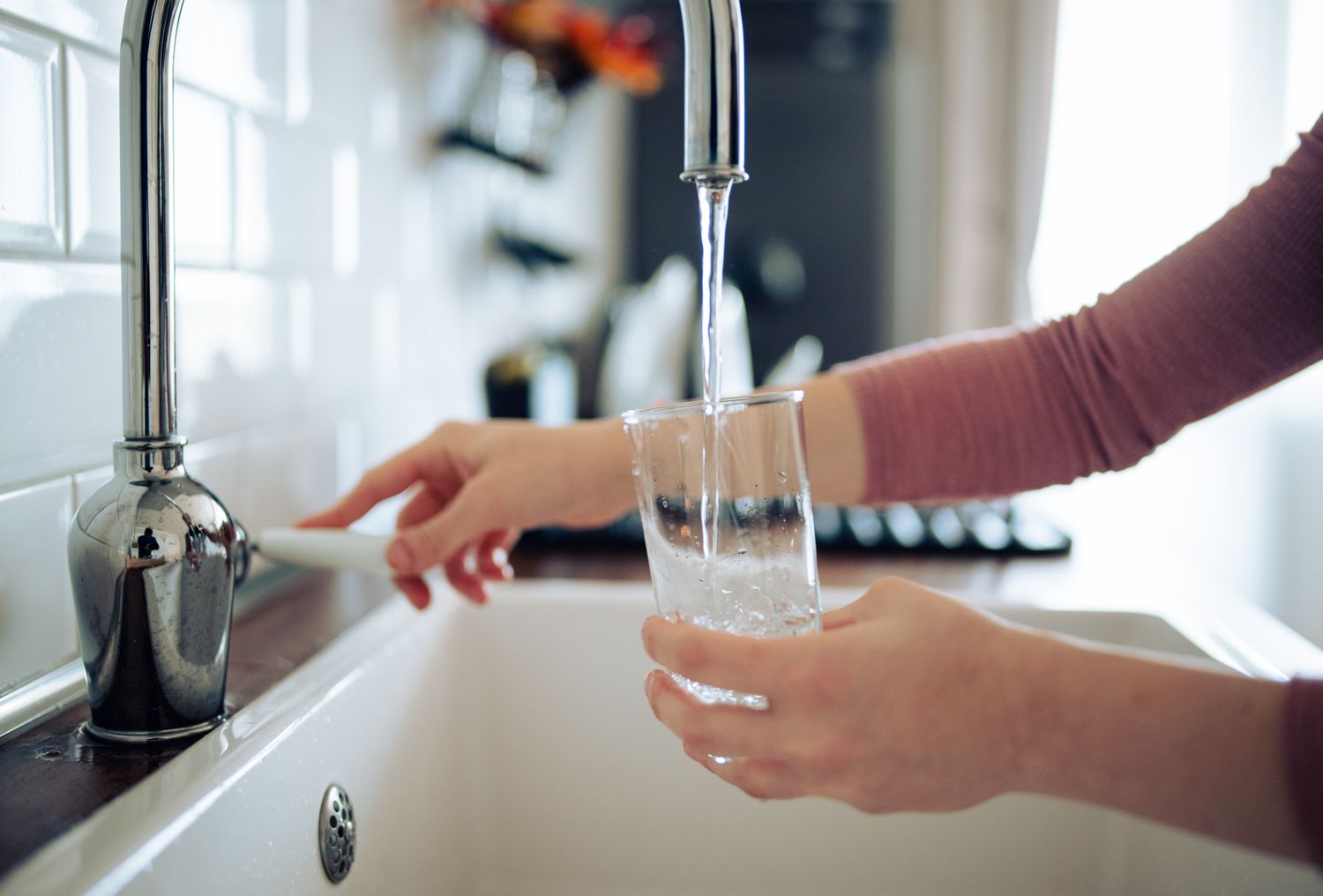 A person filling a glass with water from a kitchen faucet