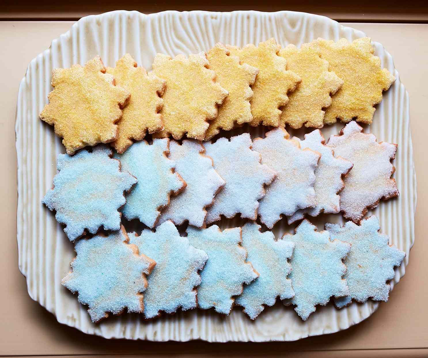 A plate of snowflakeshaped sugar cookies in pastel colors arranged in rows