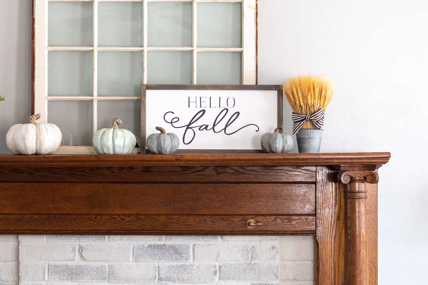 A wooden mantle adorned with pumpkins a Hello Fall sign and a bundle of wheat in a tied ribbon