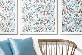 Three framed floral pattern artworks on a wall above a wooden bench with blue and white cushions
