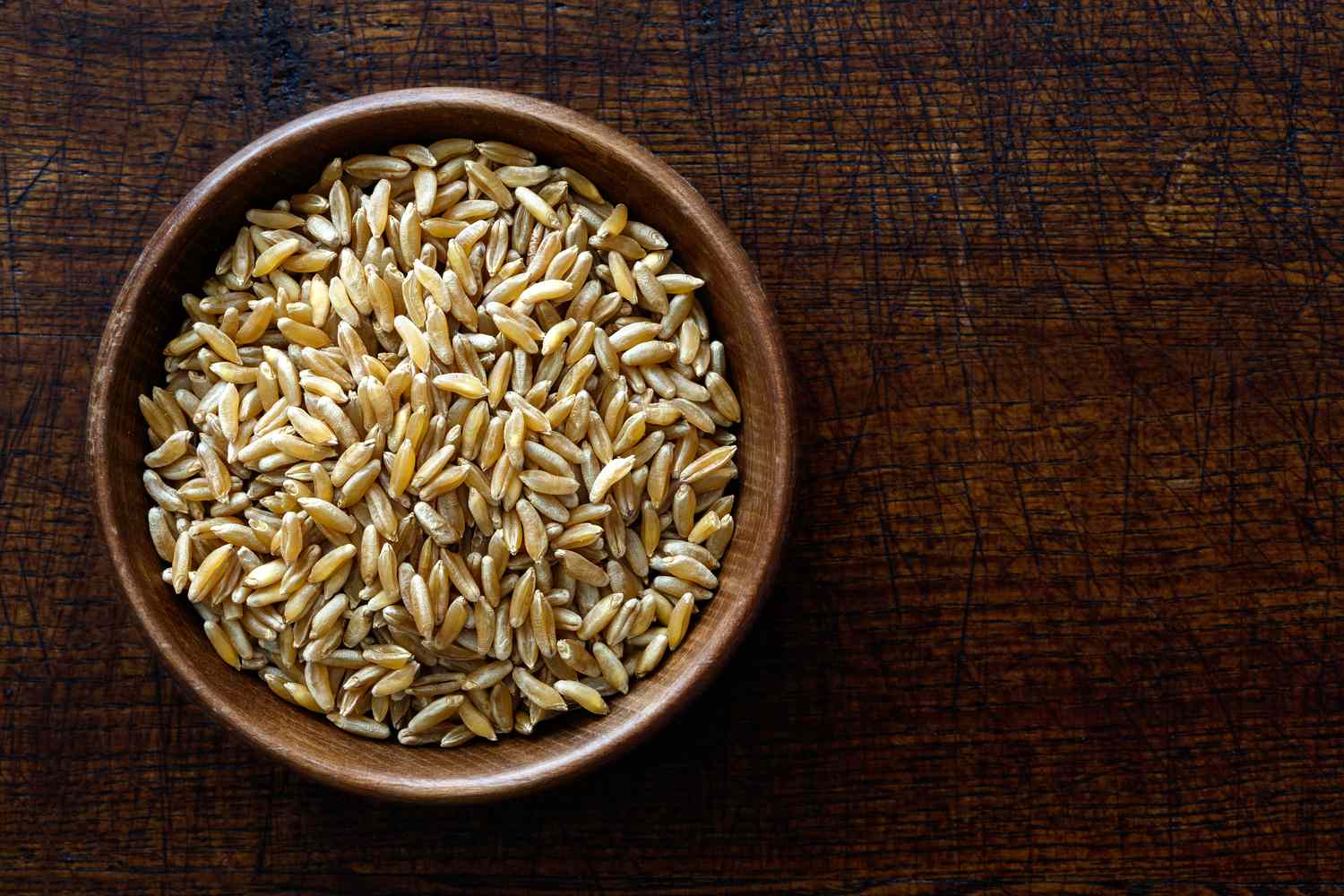 uncooked kamut wheat kernels in wood bowl on dark wooden surface