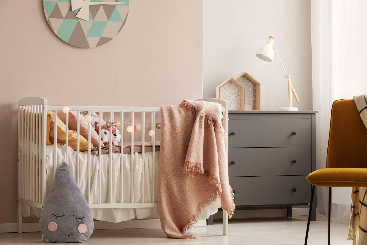 Pillows and toy in white wooden crib with pastel pink blanket in bright nursery