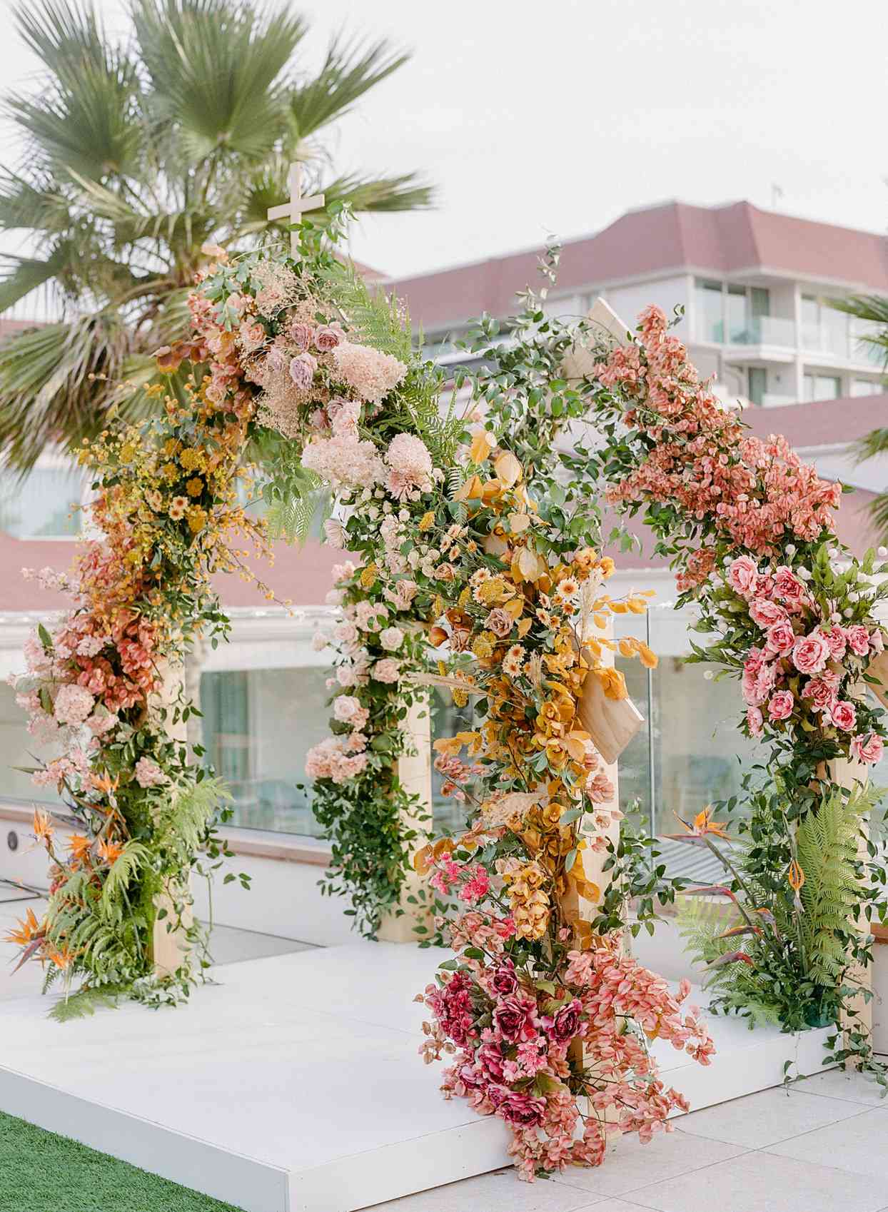 wedding ceremony arch with flowers up the sides and a cross on top