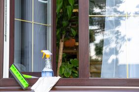 Cleaning supplies placed on a windowsill indoors including a spray bottle squeegee and cloth