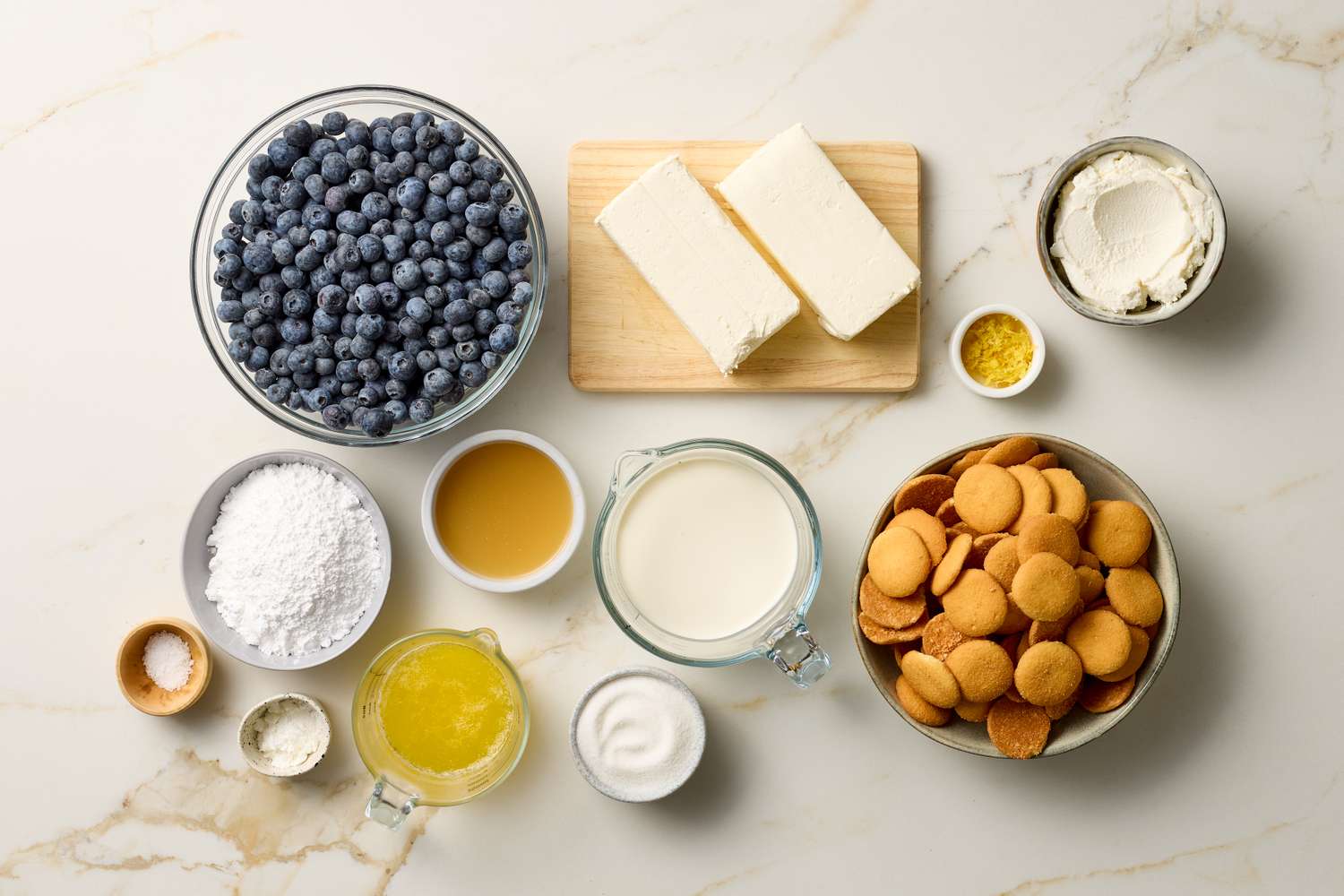 Ingredients for a nobake ricotta blueberry cheesecake arranged on a countertop including blueberries ricotta cream cheese and vanilla wafers
