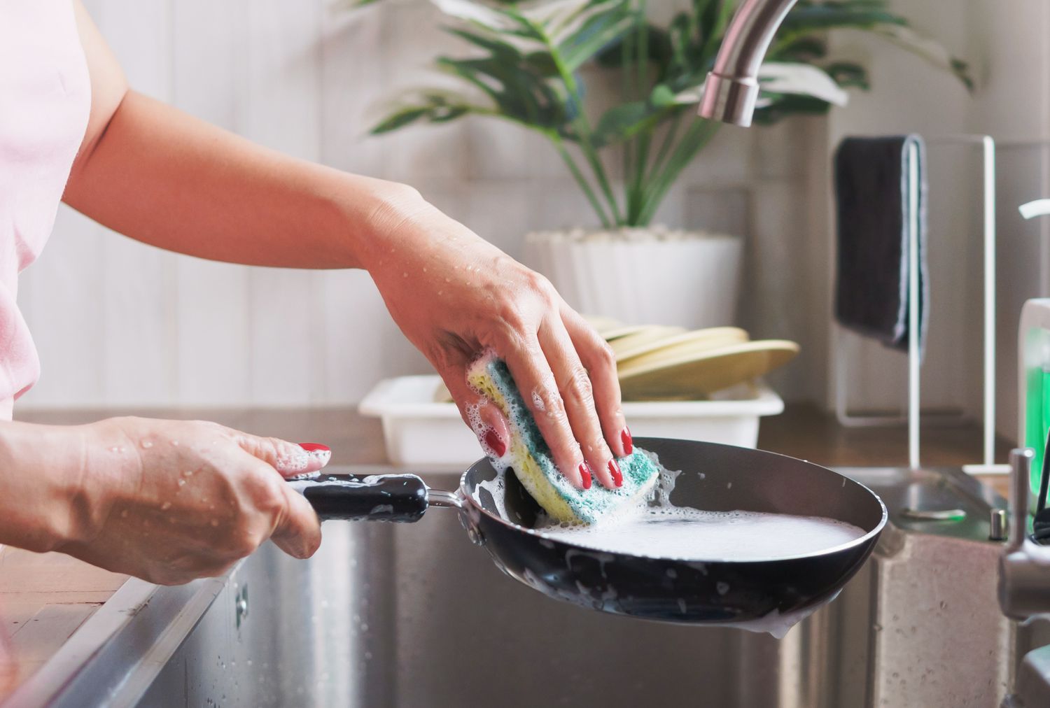 A person using a sponge to wash a frying pan in a kitchen sink