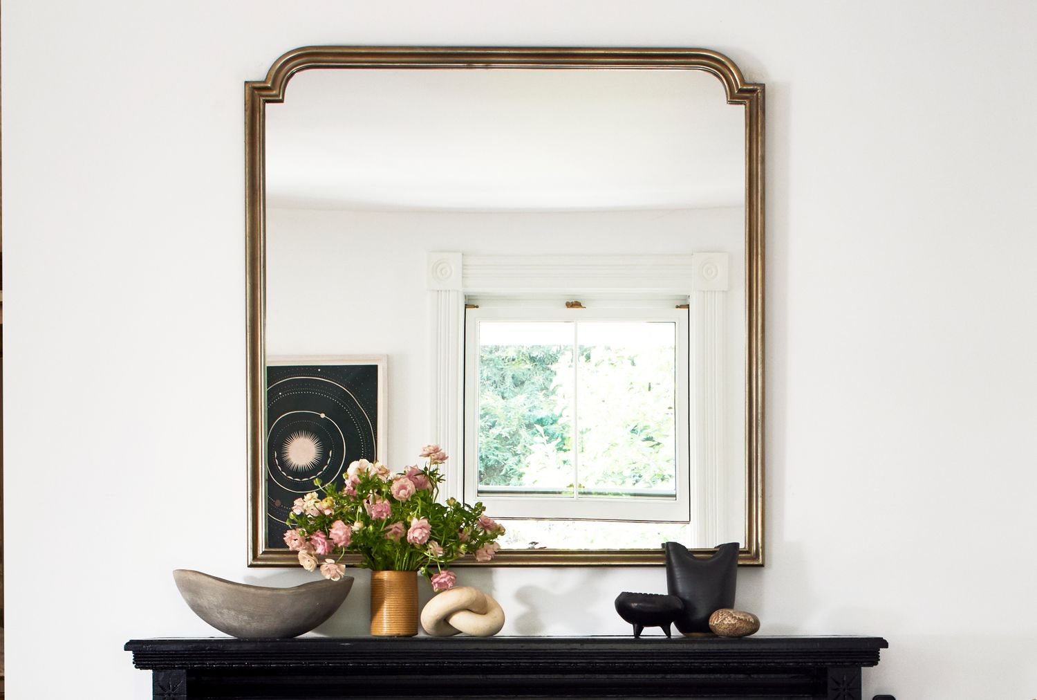 A mantle with decorative items and a vintagestyle mirror hanging above it