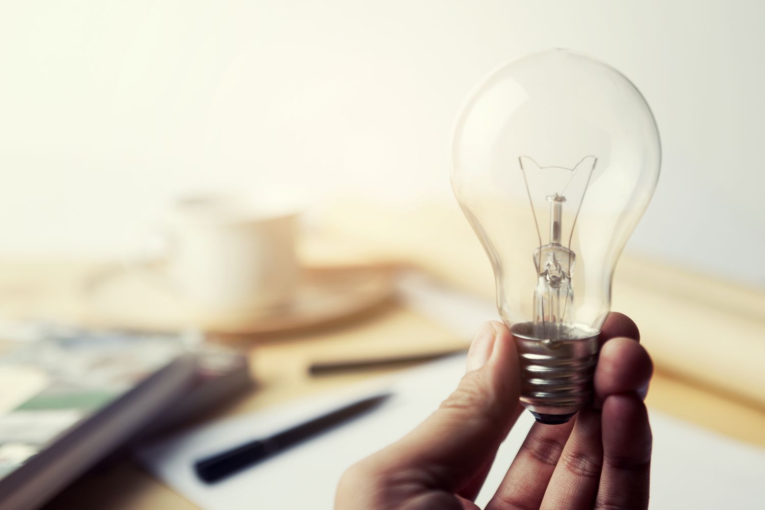 Hand holding Incandescent Lighting bulb on wooden workspace table