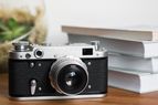 A vintage camera placed on a wooden surface with a stack of books and a glass decorative object in the background