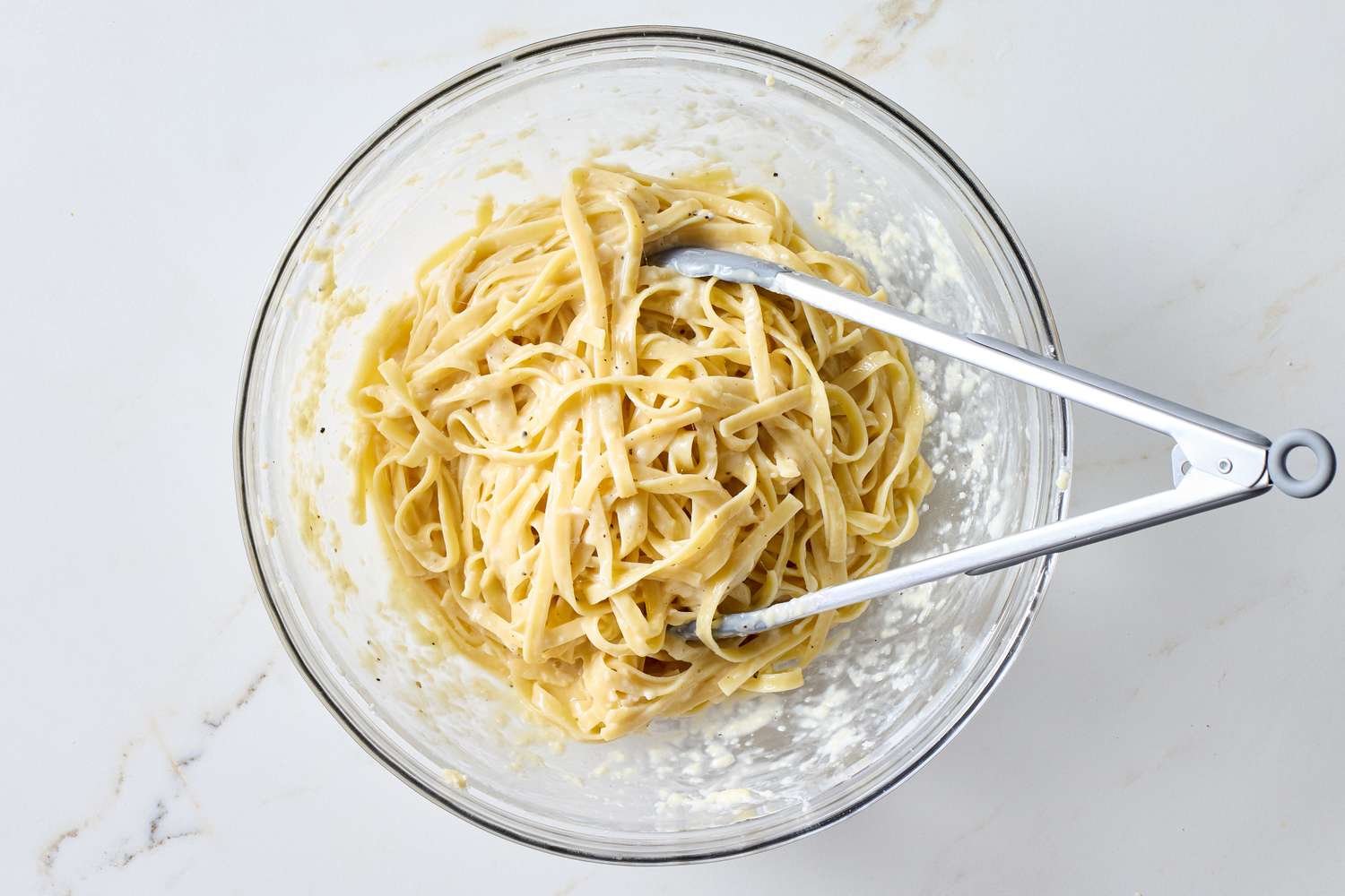 A bowl of fettuccine pasta being mixed with sauce using tongs