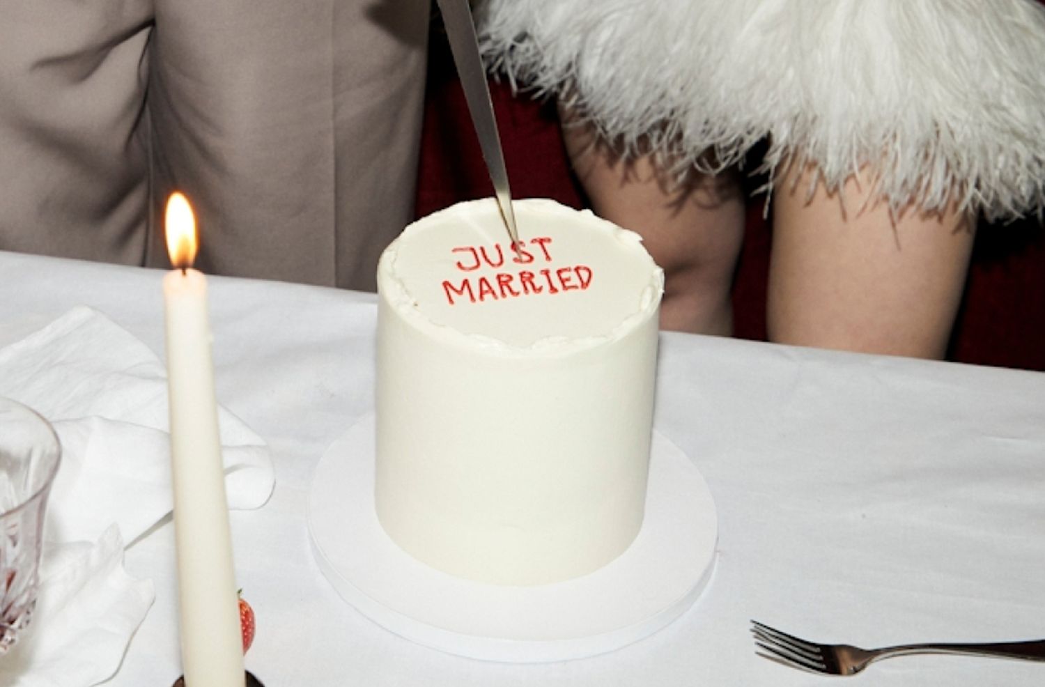 A wedding cake with the words Just Married being cut on a table with candles