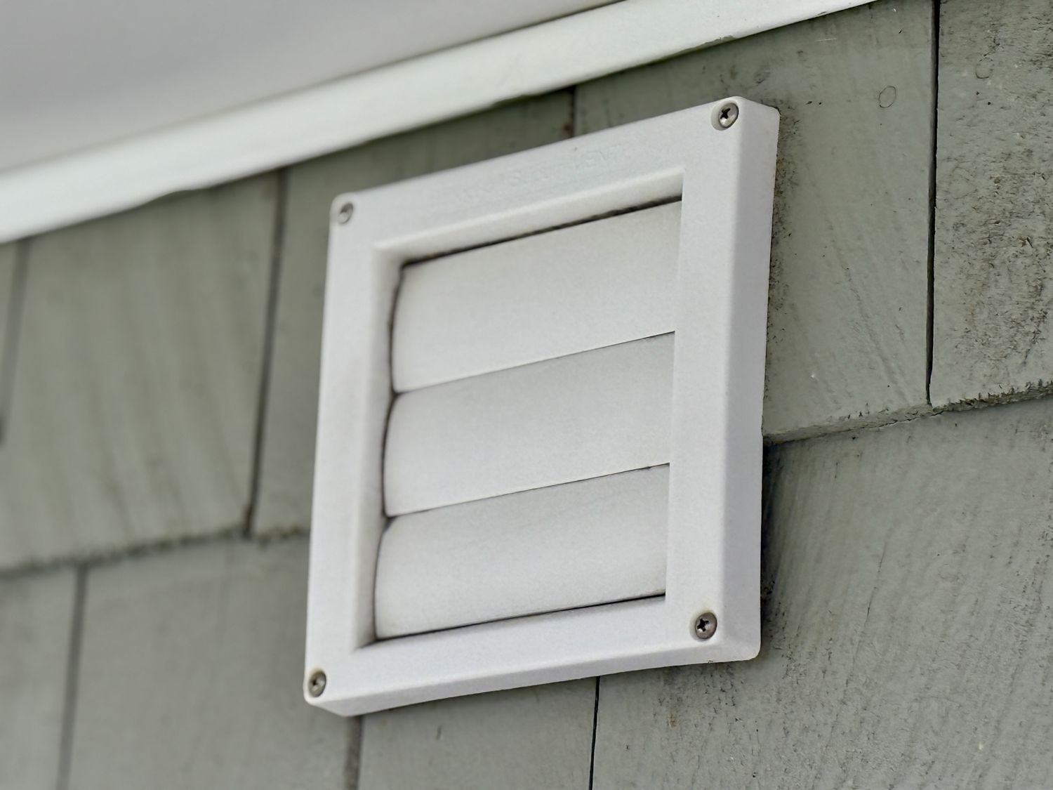 A closeup view of a white exterior vent installed on the wall of a building