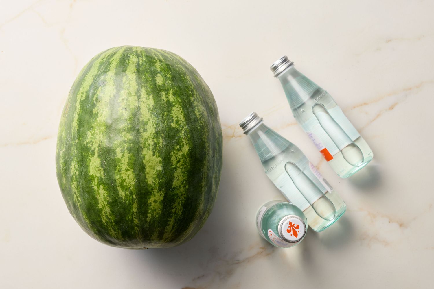 Whole watermelon with soda bottles on a marble surface