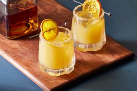 two whiskey sours and bottle of whiskey on wooden cutting board