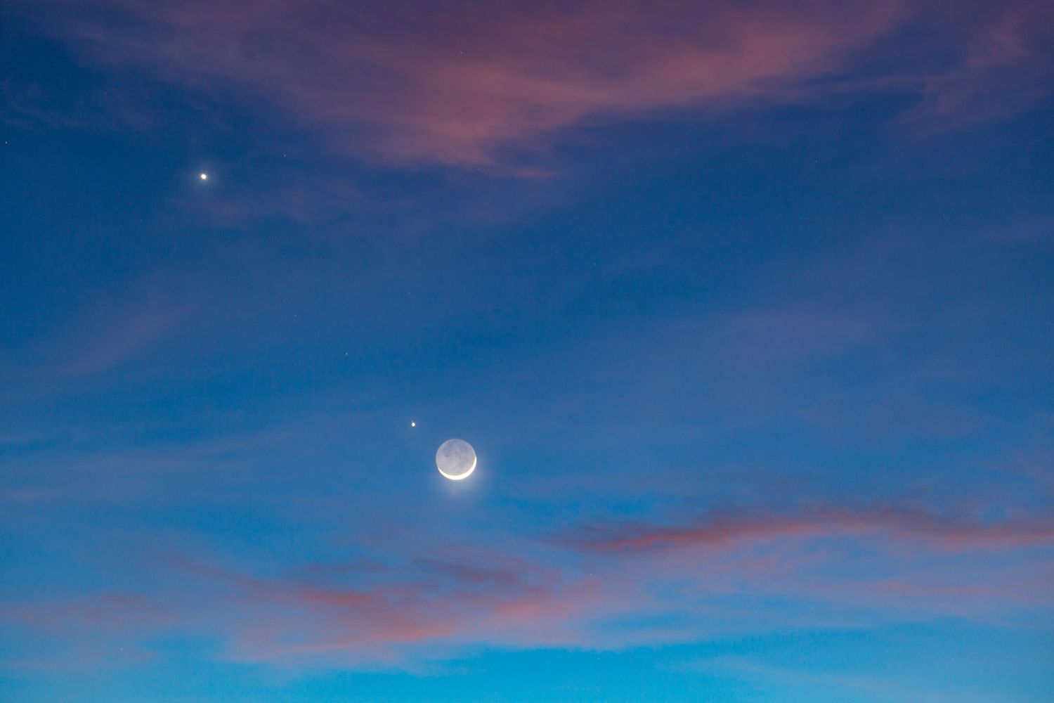 Night sky featuring the crescent moon and visible planets surrounded by soft clouds