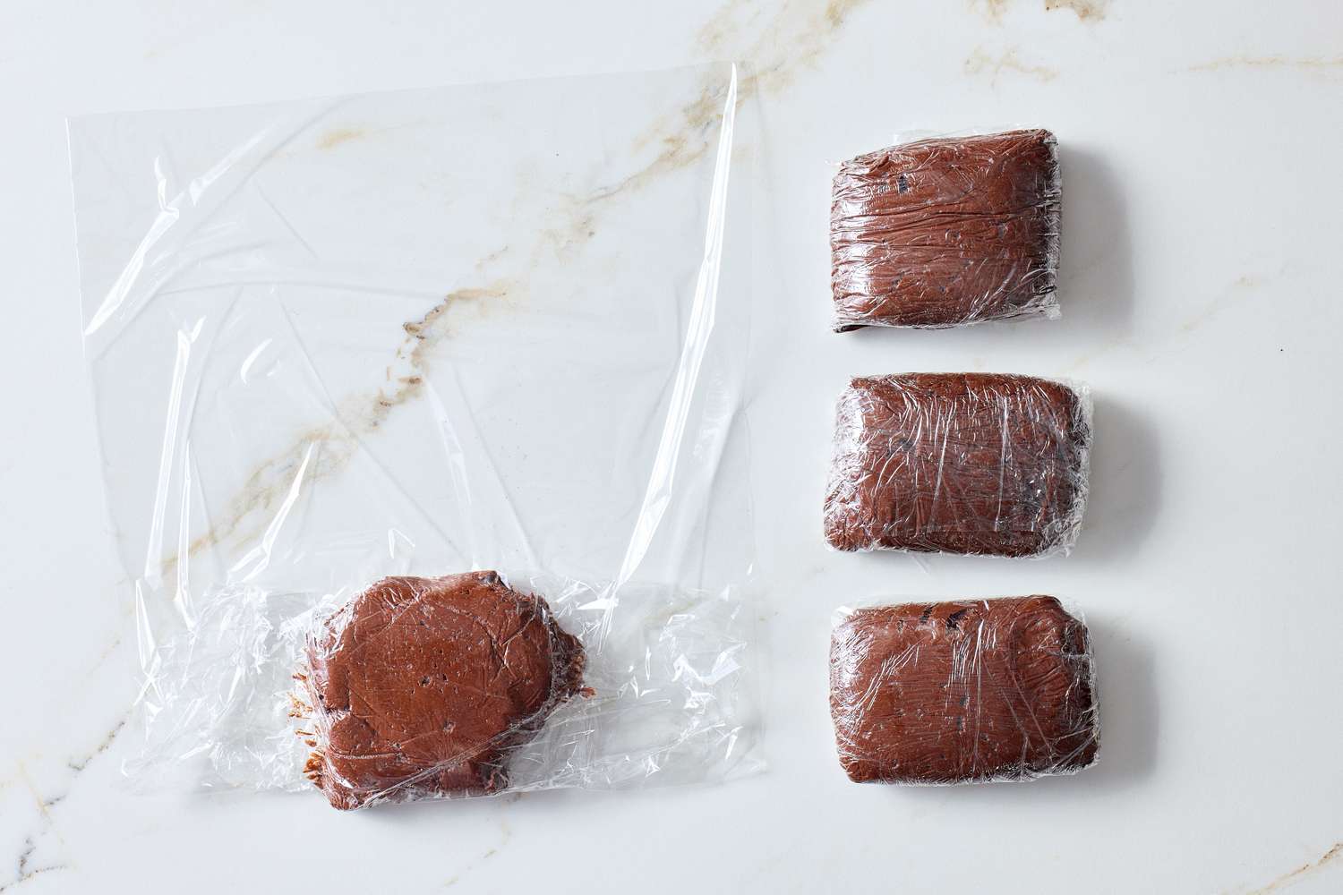 Cookie dough divided into portions and wrapped in plastic wrap for preparation