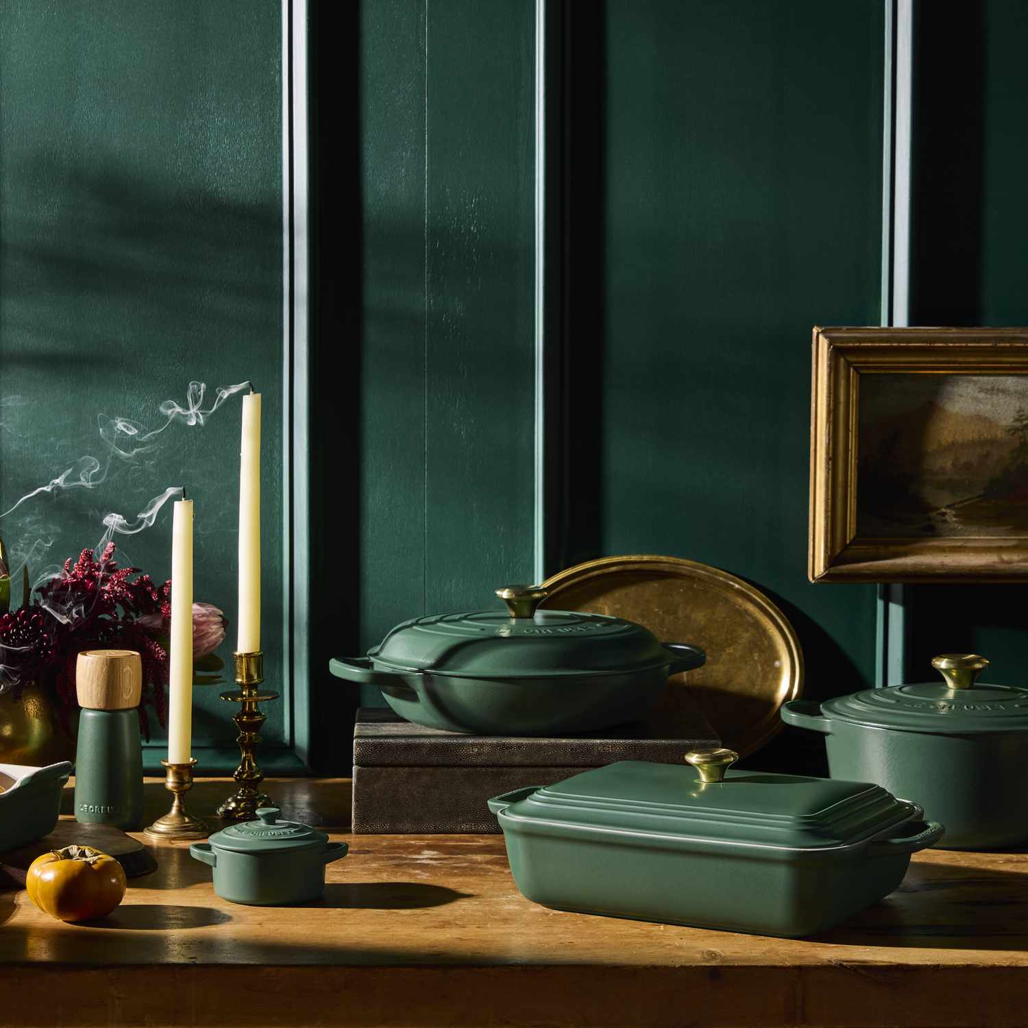 A kitchen setup with cookware candles and decorations on a wooden surface in front of a dark paneled wall