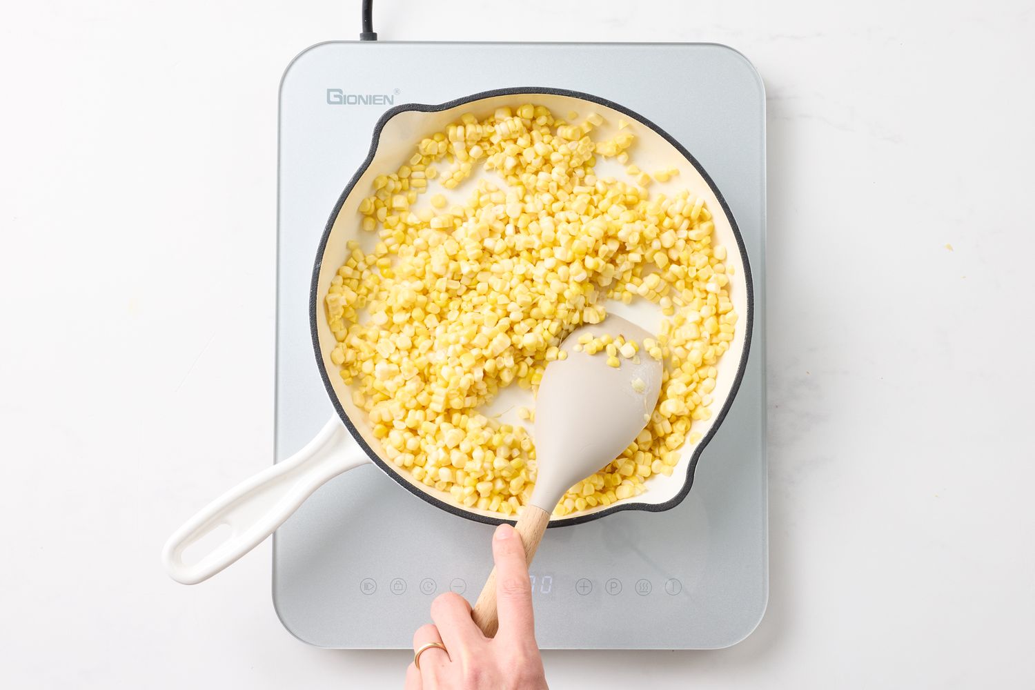 Person stirring corn in a pan on an induction stove